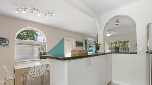 Une cuisine moderne avec des meubles blancs, un îlot central et un coin repas avec des chaises blanches.