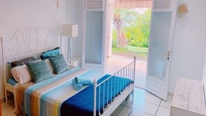 A bedroom with a bed, bedside table, lamp, and a view of a garden through an open door. - Exceptional property in a lush setting (Case-Pilote)