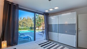 A bedroom with a large bed, a sliding glass door leading to a pool area, and a wardrobe.