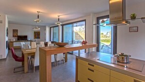 A modern kitchen with a wooden island, large windows, and a dining area with red chairs.