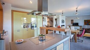 A modern kitchen with a glass-top island, built-in appliances, and a dining area with a wooden table and chairs.