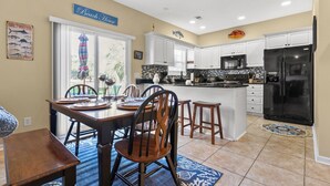 A kitchen with white cabinets, a black refrigerator, and a dining area with a wooden table and chairs. - Modern golf course townhome w/pool, close to many golf courses, shops, restaurants in North Myrtle (North Myrtle Beach)