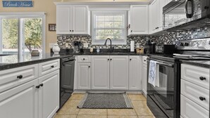 A kitchen with white cabinets, a black countertop, a tiled backsplash, and a window with blinds. - Modern golf course townhome w/pool, close to many golf courses, shops, restaurants in North Myrtle (North Myrtle Beach)