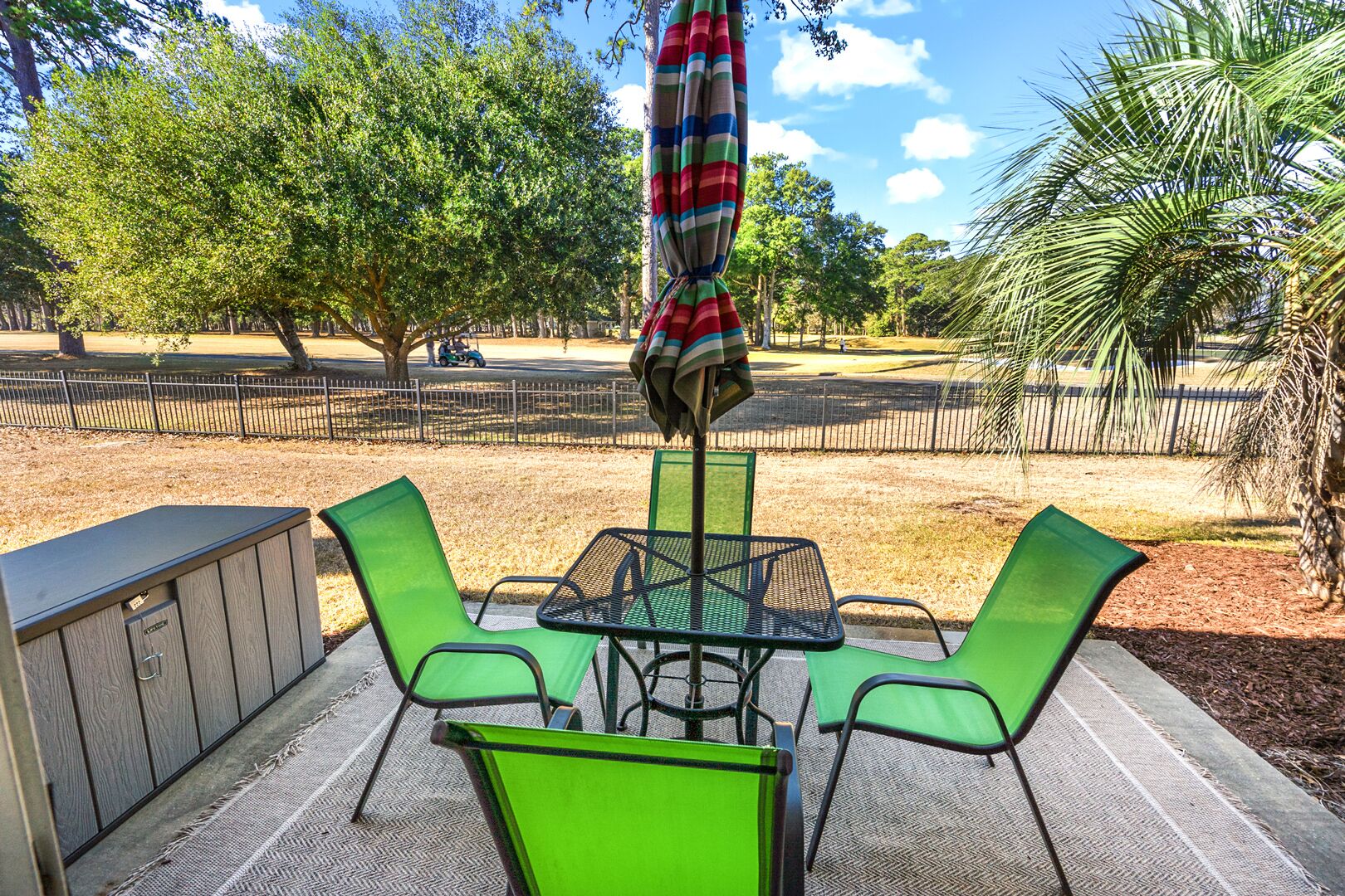 An outdoor patio with a table and chairs, a striped umbrella, and a wooden fence in the background.