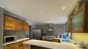 A modern kitchen with wooden cabinets, stainless steel appliances, a white countertop, and a clock on the wall. - Charming chalet in Les Praz de Chamonix near the Flégère's cable car (Chamonix-Mont-Blanc)