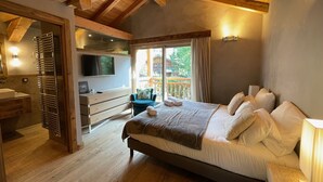A bedroom with a large bed, wooden ceiling beams, a TV, a desk, and a view of the outdoors. - Charming chalet in Les Praz de Chamonix near the Flégère's cable car (Chamonix-Mont-Blanc)