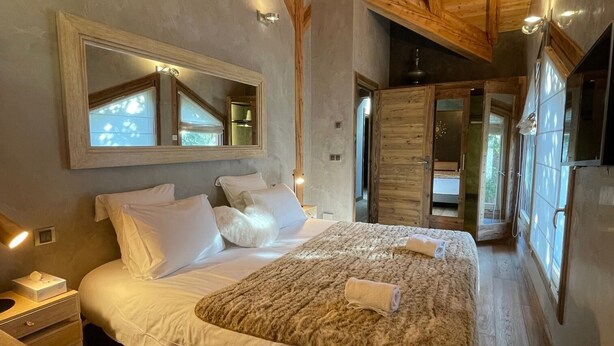 A bedroom with a large bed, wooden ceiling beams, a mirror, and a nightstand. - Charming chalet in Les Praz de Chamonix near the Flégère's cable car (Chamonix-Mont-Blanc)
