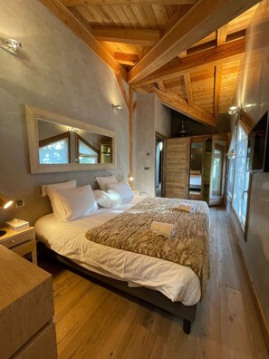 A bedroom with a large bed, wooden ceiling beams, a mirror, and a nightstand.