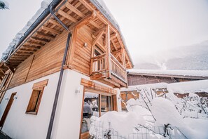 A wooden chalet with a balcony and a view of snow-covered mountains.