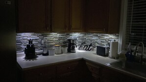 Una cocina con armarios de madera, salpicadero de azulejos y varios electrodomésticos, incluyendo una cafetera y un tostador.