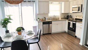 Cozinha moderna com armários brancos, eletrodomésticos de aço inoxidável e área de refeições com mesa redonda e cadeiras.