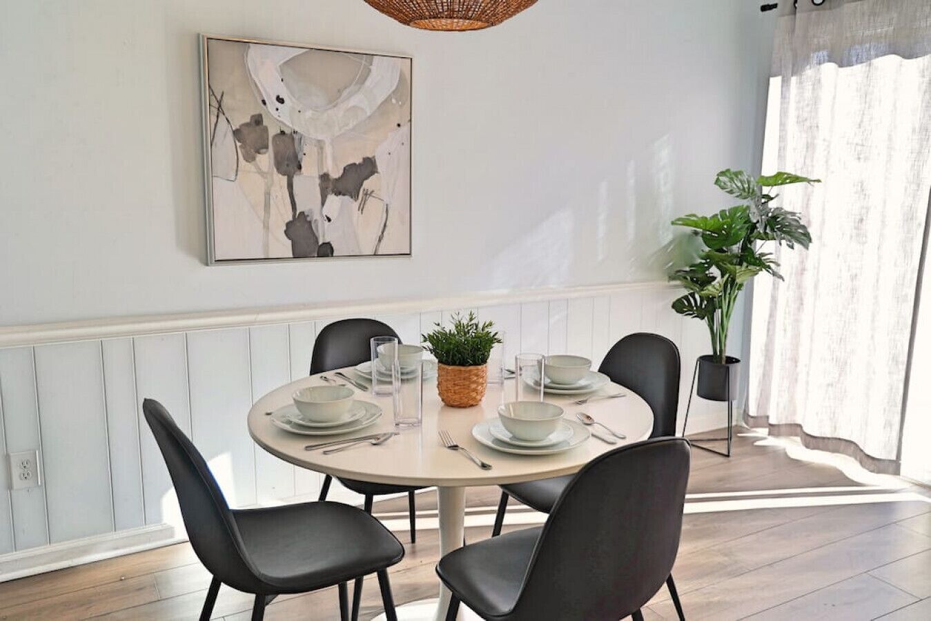 Een eetruimte met een ronde tafel voor vier personen, omringd door zwarte stoelen. Een groot abstract schilderij hangt aan de muur boven de tafel.