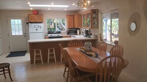 Una cocina con gabinetes de madera, una isla central con taburetes, una mesa de comedor y vistas al exterior.