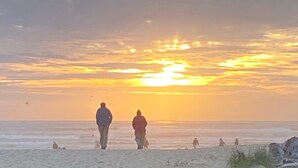 Escena de playa con gente caminando por la orilla al atardecer.