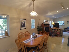 A dining area with a wooden table and chairs, a chandelier, a framed picture on the wall, and a television in the background.