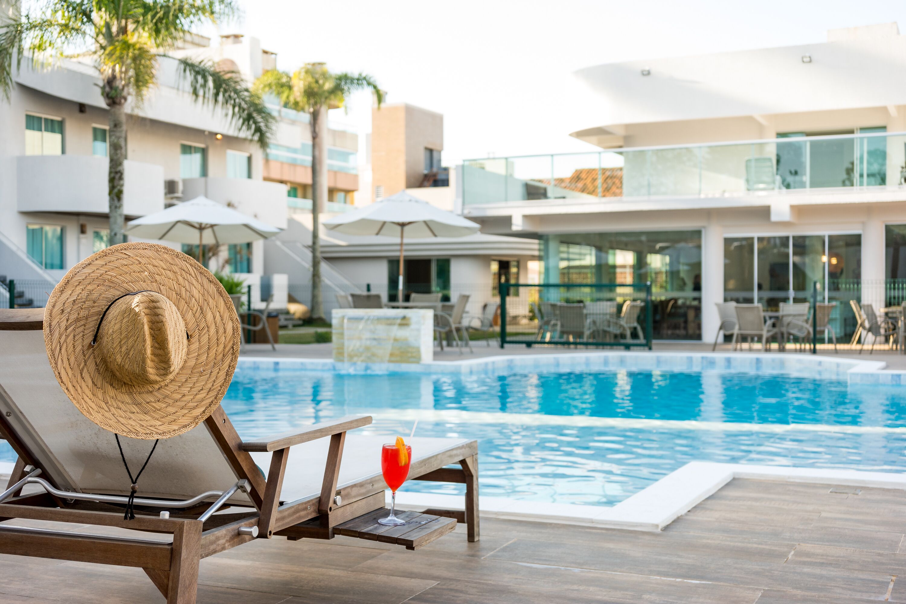 Zona de piscina con una tumbona, un sombrero de paja y una bebida.