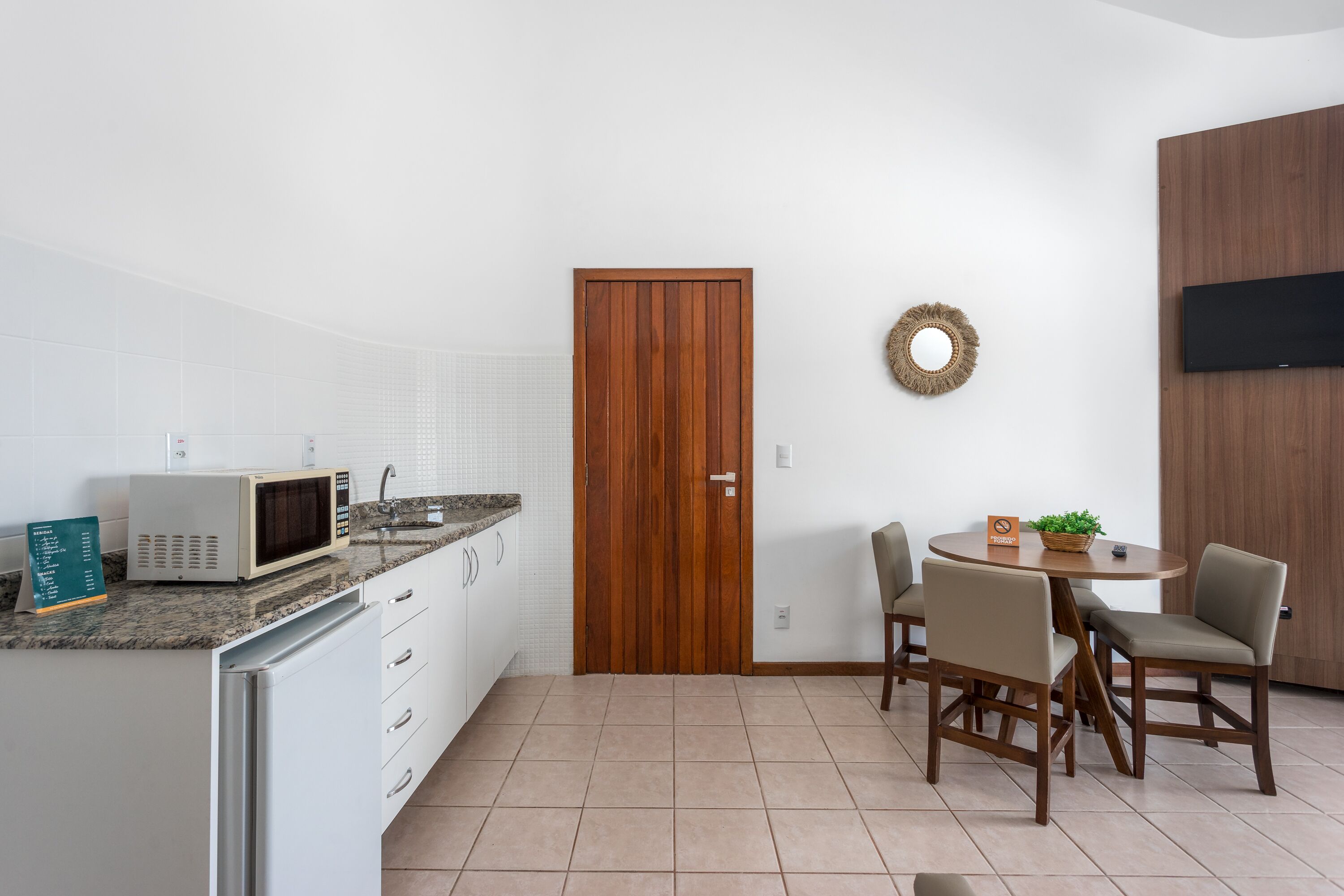 A compact kitchen with white cabinets, a microwave, and a wooden door. There is a small dining area with two chairs and a table.
