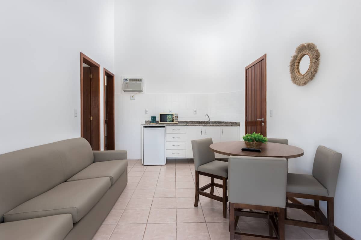 A compact living space with a sofa, dining table, chairs, a kitchenette, and a small refrigerator.