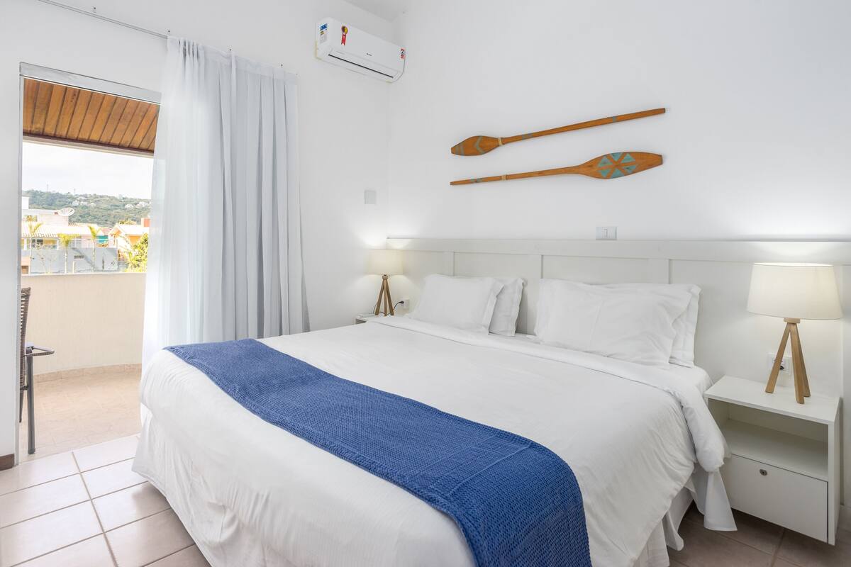 A hotel room with a large bed, two bedside tables with lamps, a view through a window, and two wooden paddles on the wall.