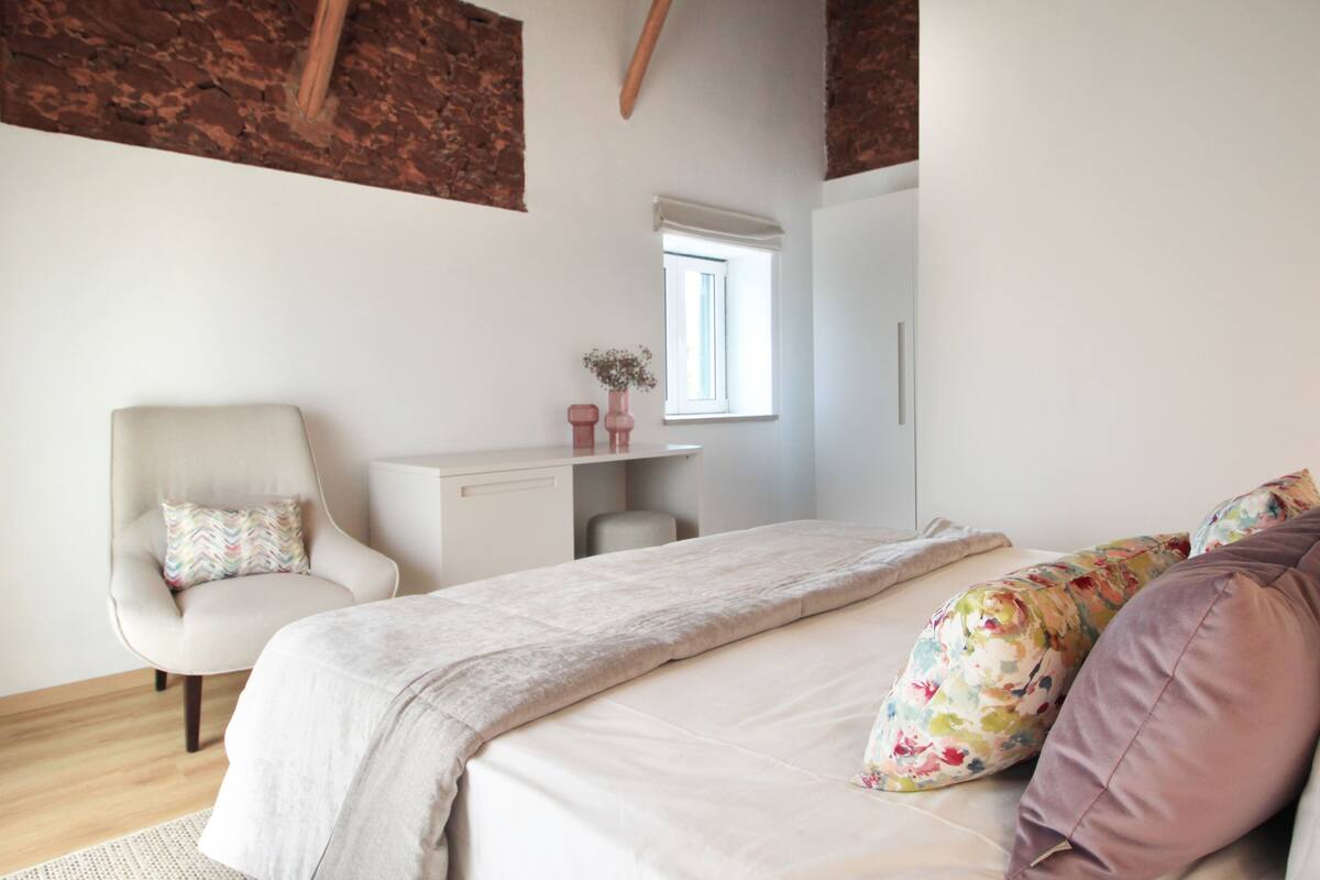 Un dormitorio con cama, una silla, un escritorio y una ventana.