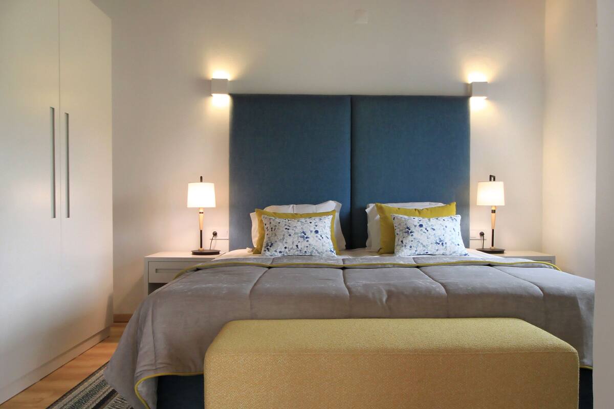 Habitación de hotel impecable con una cama grande, dos mesitas de noche y un banco al pie de la cama.