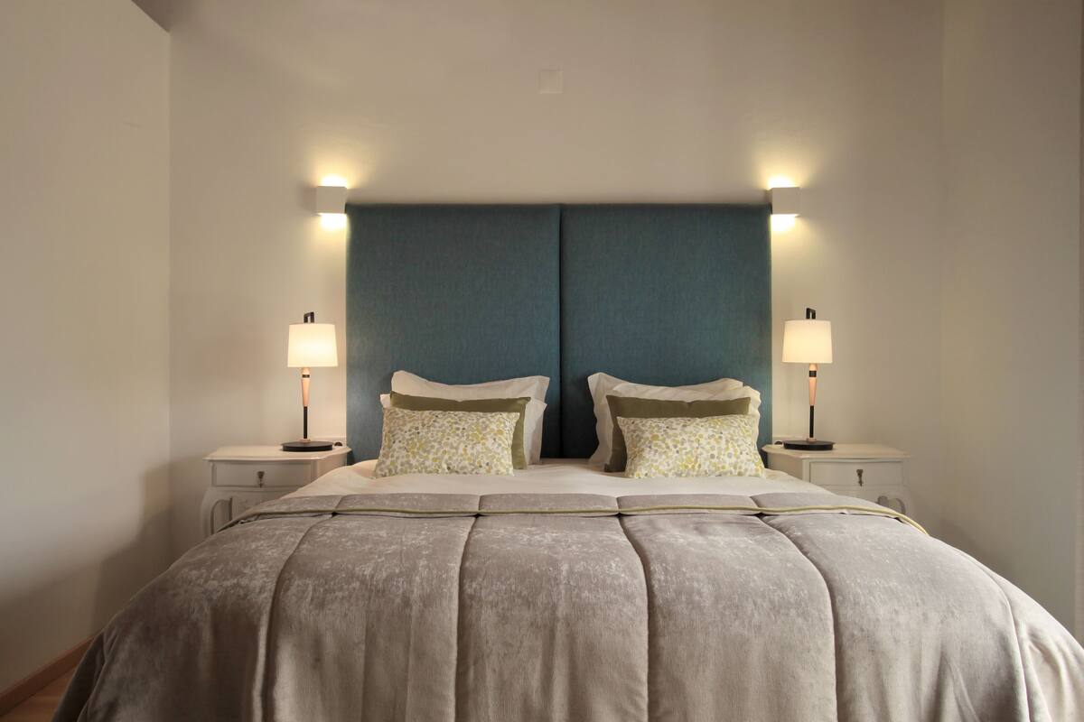 Un dormitorio con una cama grande, dos mesitas de noche y dos lámparas de pared.