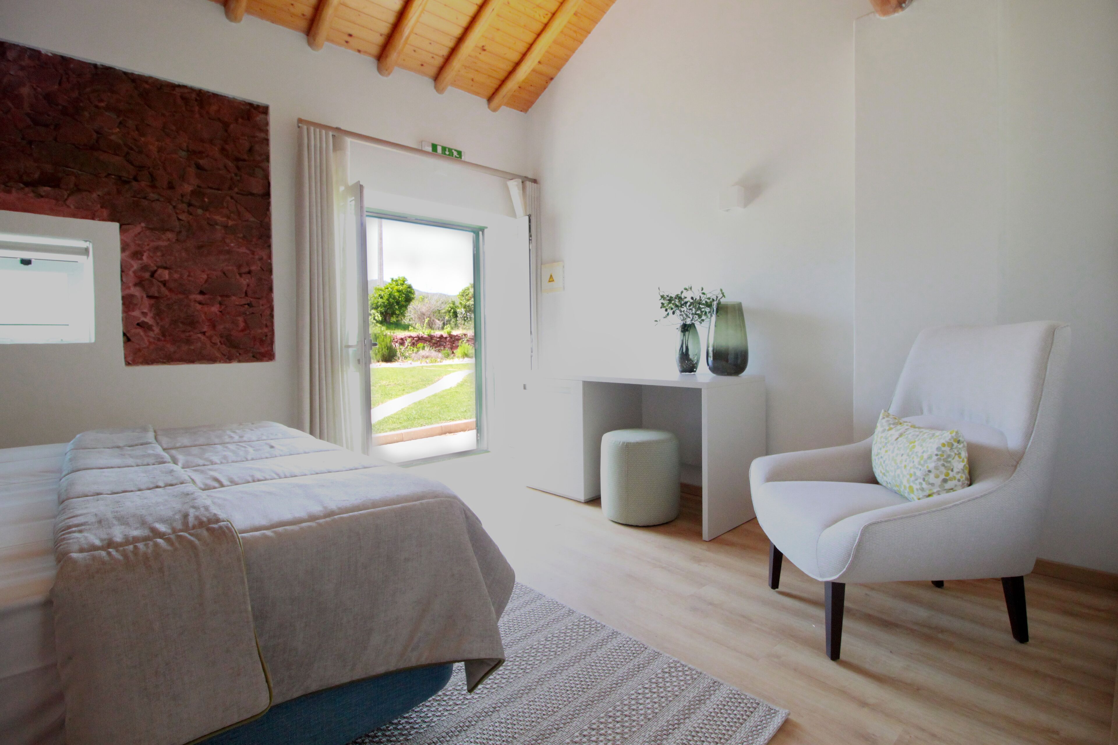 A bedroom with a bed, a chair, a desk, and a view of the outdoors.