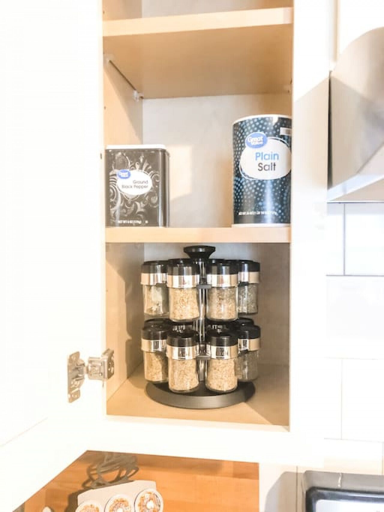A kitchen cabinet with spice containers and a canister of plain salt.