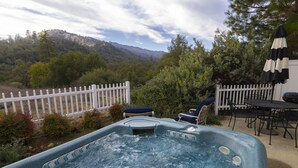 A hot tub with a view of a mountainous landscape, surrounded by a white picket fence, outdoor furniture, and a barbecue grill. - The Funky Chicken - Hot Tub - BBQ - Sleeps 4 (Ahwahnee)