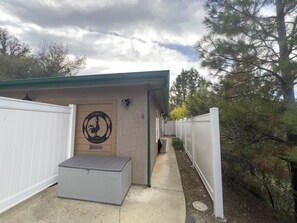 Un espace extérieur abrité comprenant un banc en béton, un mur orné d’un logo représentant un coq et une clôture blanche.