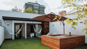 Een modern buitengebied met een houten jacuzzi, een hangmat en een glazen deur naar een kamer.