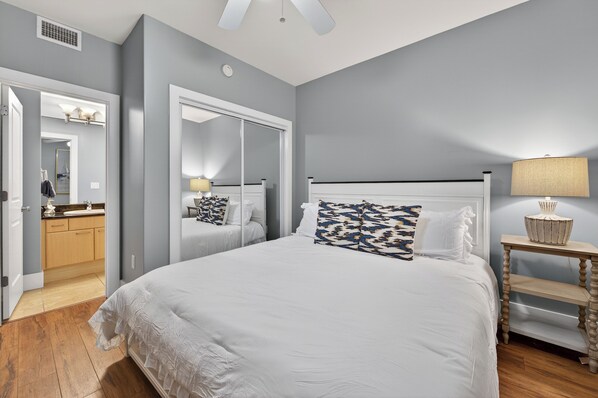 A bedroom with a large bed, a nightstand, a mirror, and a door leading to a bathroom. - DOWN BY THE BAY! Gulf Facing unit! ASK ABOUT DISCOUNTS!! (Orange Beach)