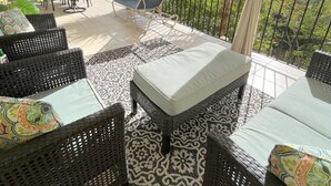 A covered outdoor seating area with wicker furniture, a patterned rug, and a view of the sea. - Echo @Serendip Vacation Condos (Cruz Bay)
