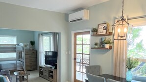 A modern living room with a dining area, a TV, and a large window with a view of greenery. - Echo @Serendip Vacation Condos (Cruz Bay)