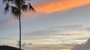 A pool area with a wooden deck, surrounded by palm trees and a view of a coastal landscape during sunset. - Echo @Serendip Vacation Condos (Cruz Bay)