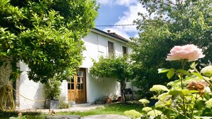 Una casa rústica amb façana blanca, porta de fusta i jardí amb una petita bassa i vegetació.