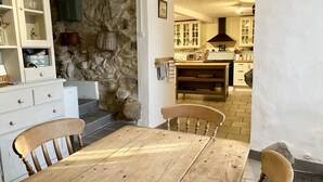Una cuina rústica amb pared de pedra, taula de fusta i armaris.
