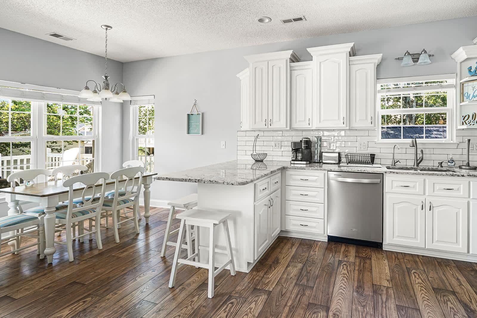 A modern kitchen with white cabinetry, a dining area with a table and chairs, and a view of greenery outside.