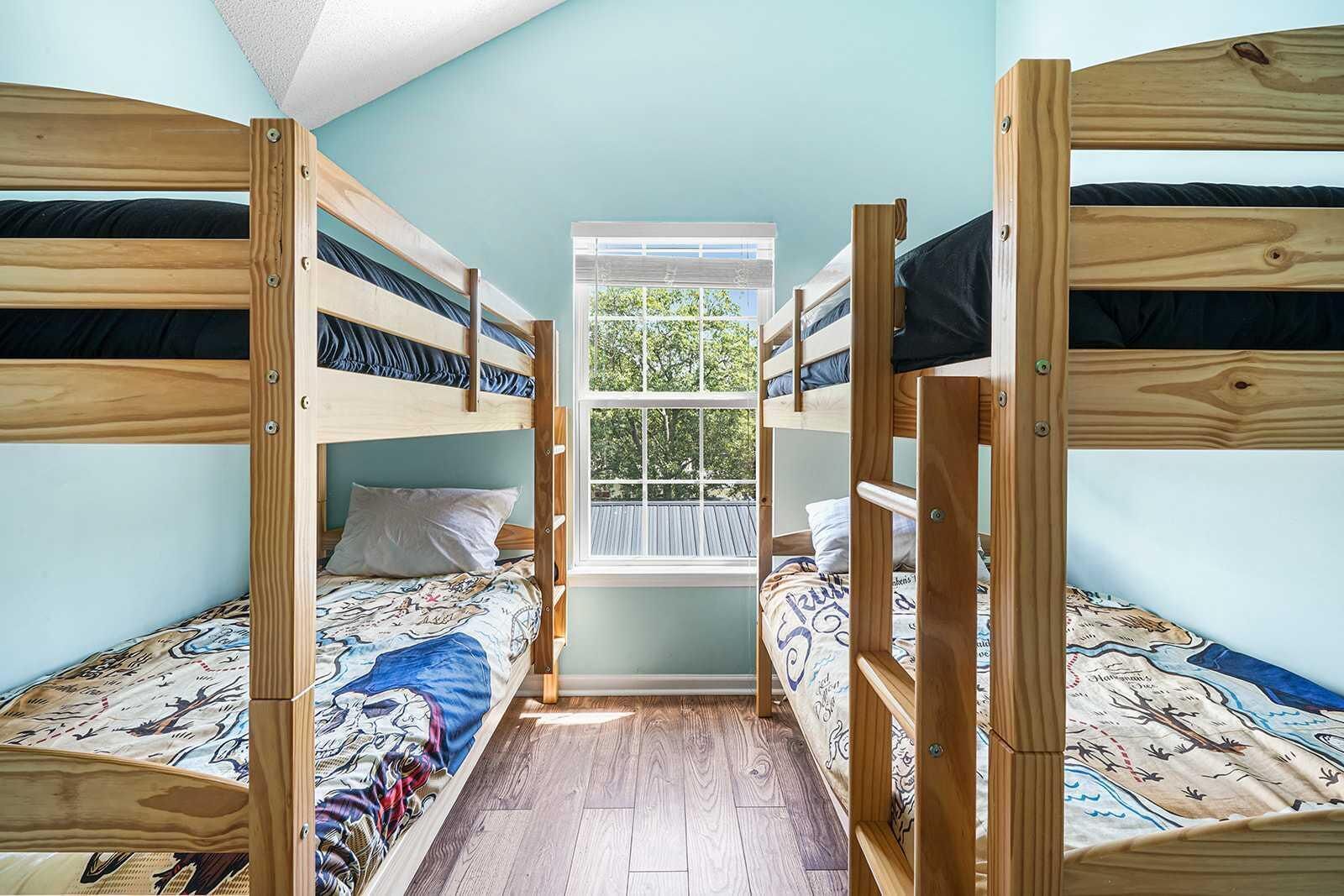 A bunk bed room with a window, wooden flooring, and a patterned bedspread.