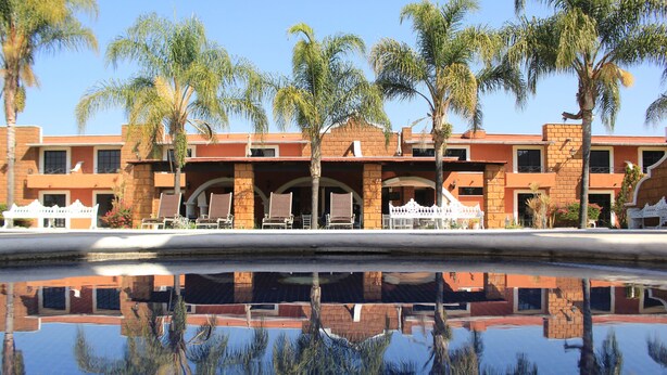 Un hotel con piscina que refleja palmeras y fachada de ladrillo.