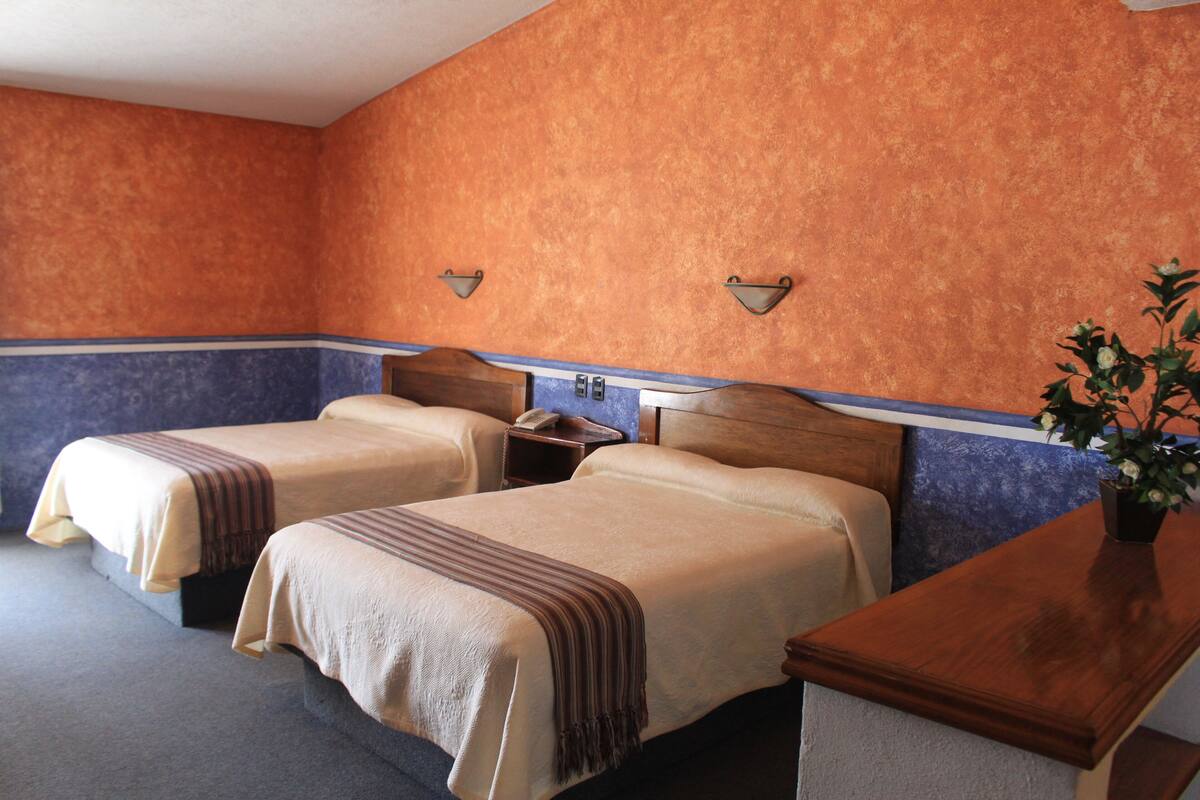 A hotel room with two beds, a wooden headboard, a nightstand, a telephone, and a potted plant.