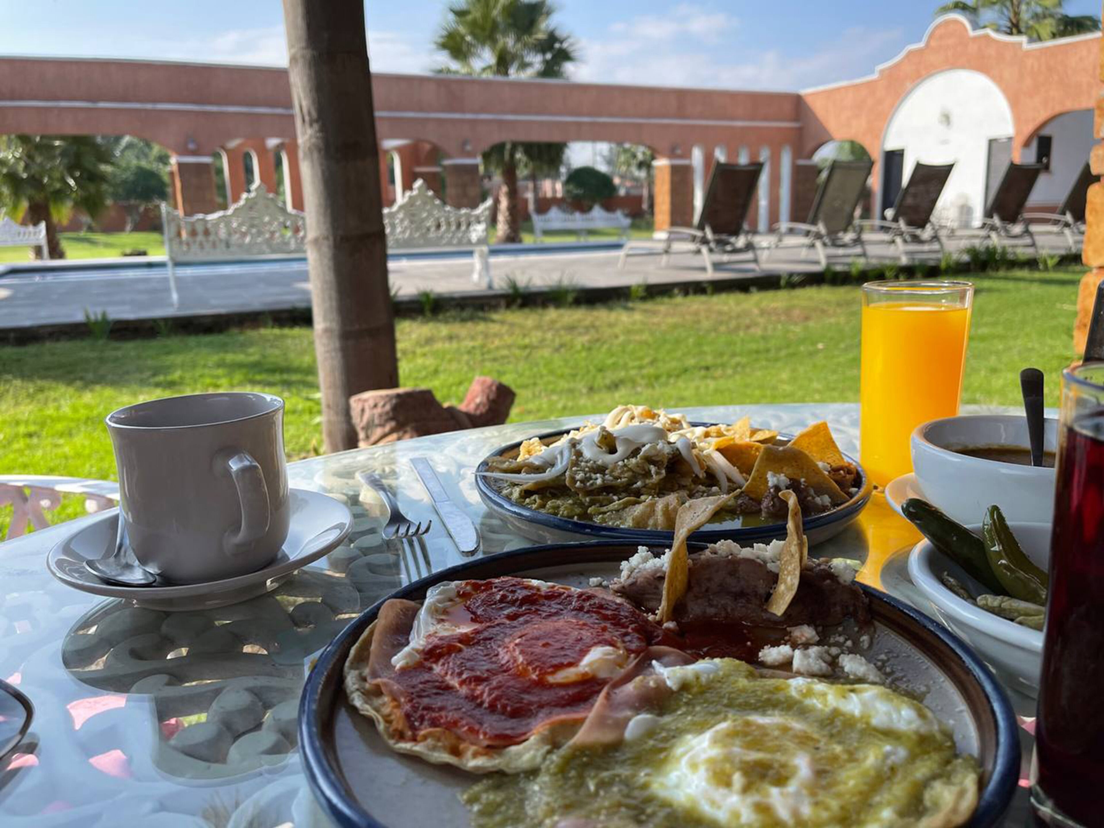 A table with breakfast items including eggs, chips, and a drink, set outdoors with a view of a pool and lounge chairs.