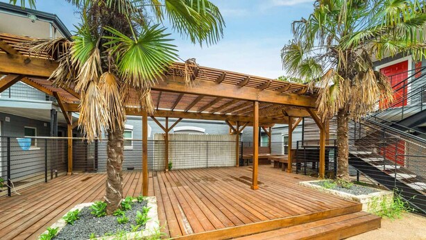 A wooden deck with a pergola, palm trees, and a stone planter with greenery. - Stylish 2BR Near UT Hyde Park Evonify (Austin)