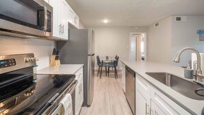 A modern kitchen with stainless steel appliances, a dining area with a table and chairs, and a view into another room. - Stylish 2BR Near UT Hyde Park Evonify (Austin)