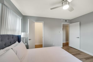 Relax in this serene bedroom with a large bed, bedside table, and window with vertical blinds.