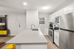Enjoy cooking in this well-equipped kitchen with a stainless steel refrigerator and oven, white cabinetry, and sleek countertops.