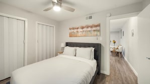 Une chambre à coucher avec un lit, un ventilateur de plafond, un tableau et, au fond, un coin repas.