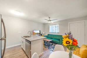 A compact living space with a kitchenette, a green sofa, a dining table, and a ceiling fan.
