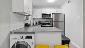 Une cuisine compacte avec des meubles blancs, un four à micro-ondes encastré, un réfrigérateur et un lave-linge.