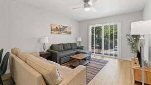 A modern living room with a sofa, coffee table, and a ceiling fan. There is a large window with a view of greenery outside. - Modern 2BR Near UT Hyde Park Evonify (Austin)